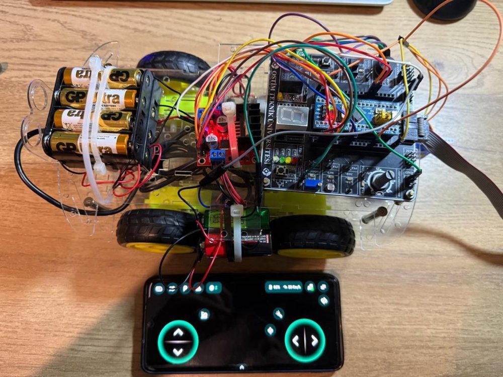 Keşif robotunun üstten görünümü: pil paketi, motor sürücü, kablolarla bağlı STM32 geliştirme kartı ve telefon kontrol arayüzü
